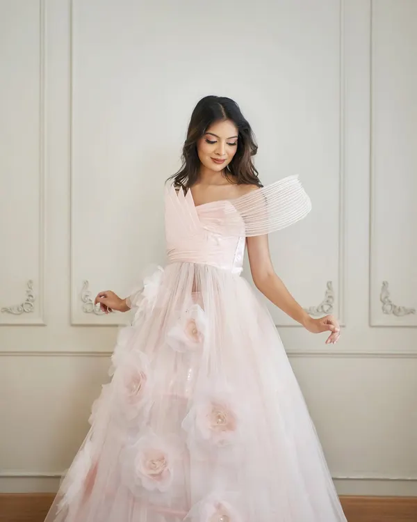 Introducing 'Carol', a dreamy pink ball gown. It features a sheer tulle skirt with 3D floral accents and a uniquely structured, wired drape on the bodice.