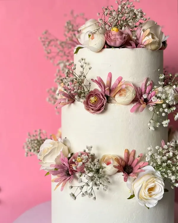 Celebrate your love with three tiers of minimalist beauty. This stunning wedding cake is adorned with fresh flowers and baby's breath, all crafted without fondant or buttercream using wholewheat flour.