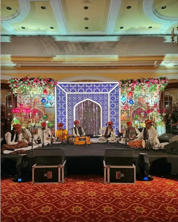 The stage for a Sufi Night, featuring a live Qawwali band. The backdrop is a custom-designed panel with intricate blue and white jaali patterns, flanked by vibrant floral arrangements to create an authentic and mesmerizing setting.