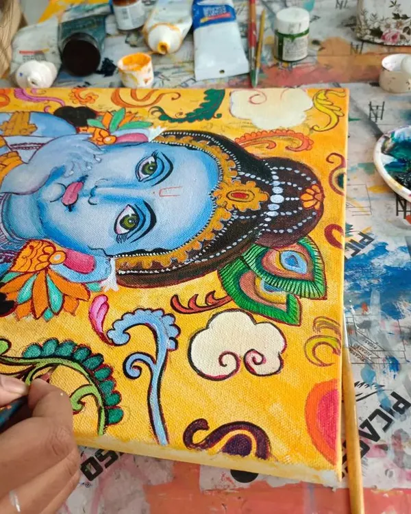 A student working on a large Kerala Mural painting, a traditional art form known for its vibrant colors and divine figures.