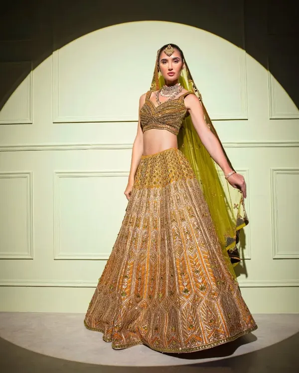 A truly regal bridal lehenga, captured in the spotlight. This opulent gold creation features extensive hand-embroidery, perfect for the bride who wants to feel like royalty.