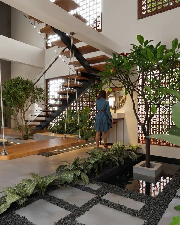 This indoor courtyard is the heart of the home, featuring a traditional wooden swing, a small water body, and lush greenery. The space is designed with jali screens and an open staircase, allowing natural light and air to flow freely, creating a tranquil atmosphere that connects the interior with nature.