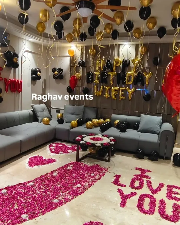 A full view of a luxurious romantic decoration package. This setup for a wife's birthday includes a dense rose petal walkway, multiple balloon arrangements on the ceiling and floor, and foil letters to display your personal message.