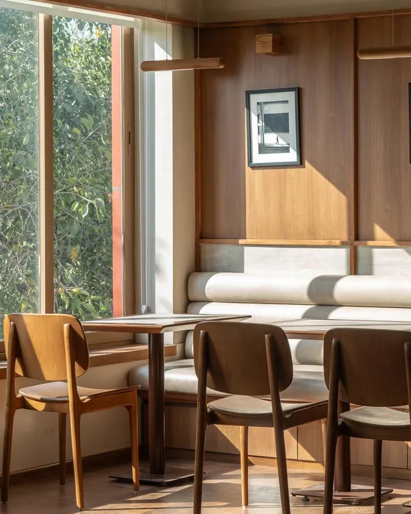 A sun-drenched corner of the cafe, where the light streams in, creating a perfect spot for a morning coffee. The design is clean and simple, allowing the quality of the light and materials to speak for themselves.