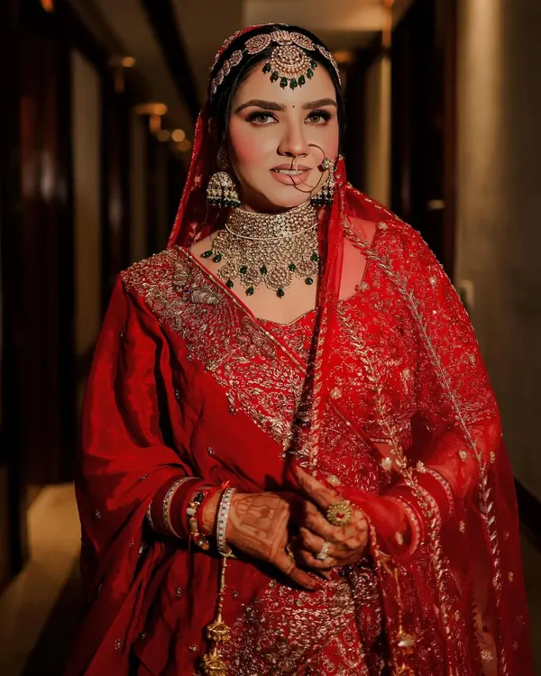 A classic bridal portrait that captures the bride's confident gaze and radiant glow. Her traditional red lehenga, intricate diamond and emerald jewelry, and elegant nath are all beautifully highlighted.