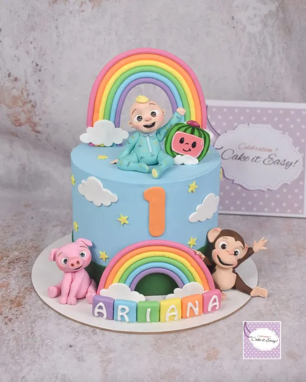 A vibrant Cocomelon cake for a first birthday, complete with JJ, the watermelon, a friendly monkey, and a pig. The double rainbow and colourful name blocks make it extra cheerful.