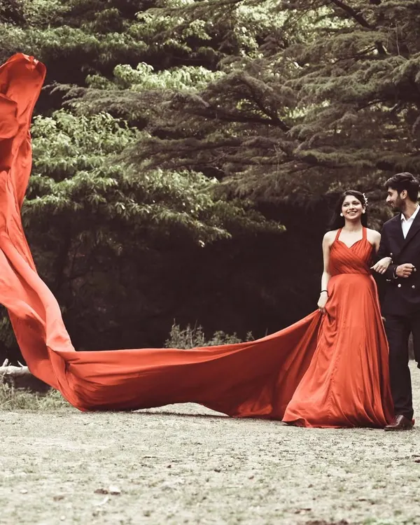 A dramatic pre-wedding portrait in a forest setting, with the bride's long red trail creating a stunning visual effect.