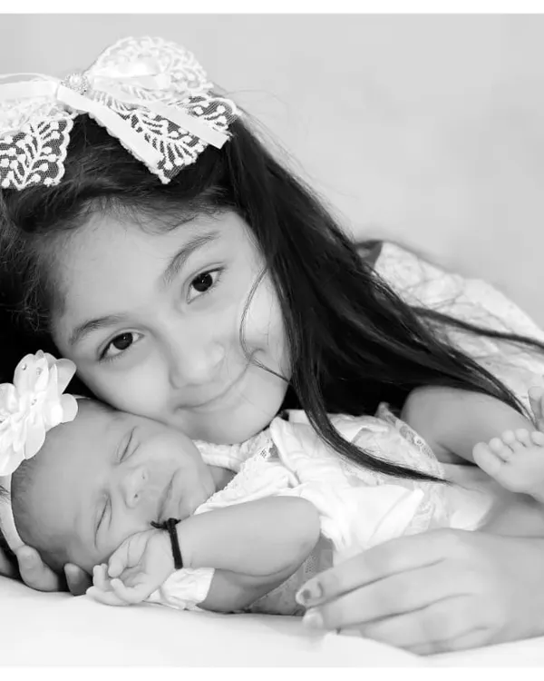 A beautiful black and white portrait capturing the gentle love of an older sister for her newborn sibling. We specialize in creating timeless family heirlooms.