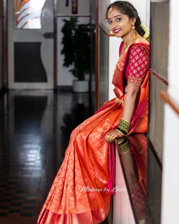 A beautiful bride ready for her Muhurtham ceremony. Her look features classic South Indian bridal makeup with a focus on radiant skin and defined eyes, paired with a stunning orange and pink silk saree.