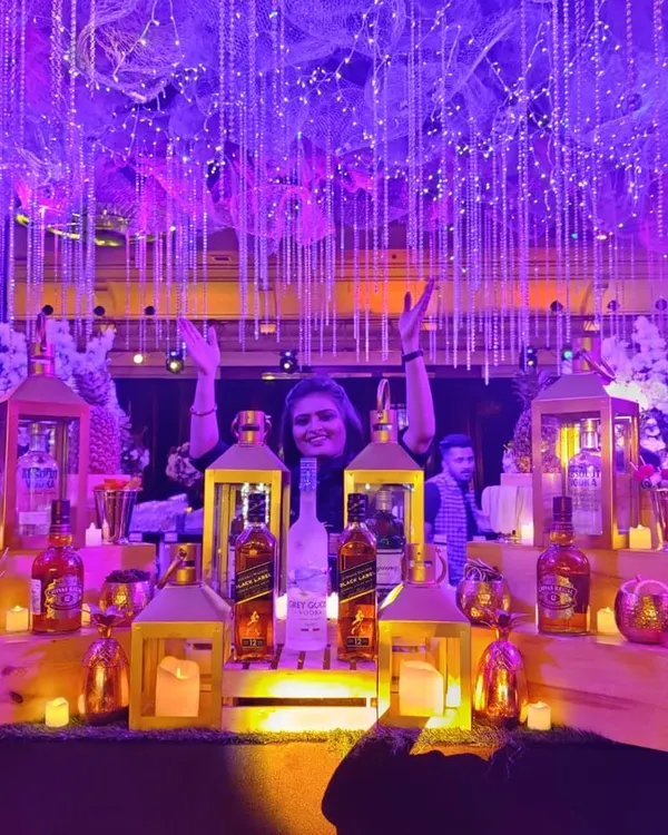 A wide shot of the spectacular Great Gatsby bar, fully lit for an evening of celebration. A happy team member celebrates behind the counter, which is adorned with lanterns, candles, and a stunning overhead light installation.