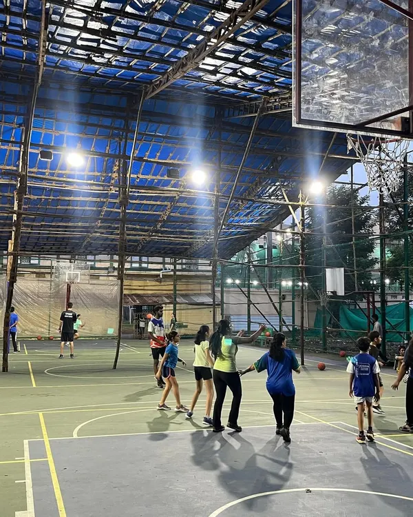 This is my covered basketball court in the heart of Bandra West, available for you to book and play. As you can see, the floodlights are on for a great evening game, and the roof ensures that your match goes on, no matter the weather.
