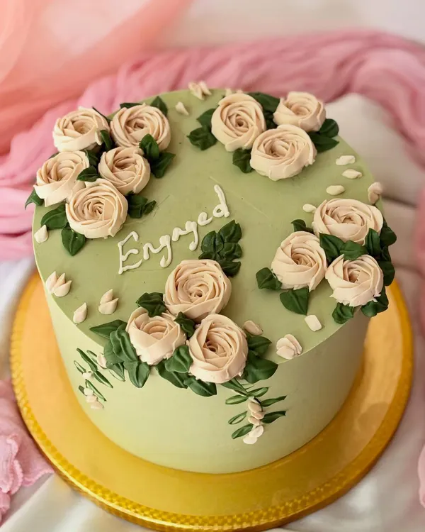 An elegant engagement cake in a beautiful sage green. The cake is adorned with hand-piped buttercream roses in a soft beige, creating a sophisticated and romantic look.