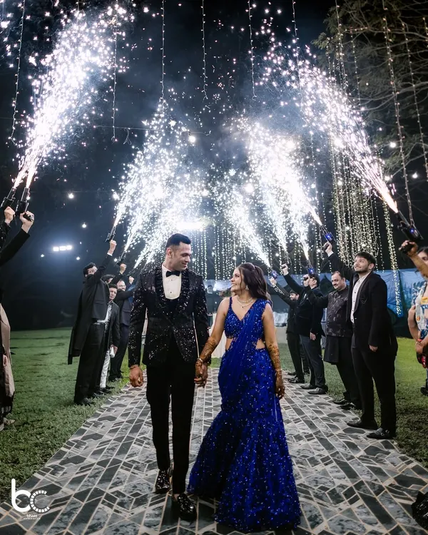 A grand entrance for a lifetime of happiness. The couple walks hand-in-hand under a brilliant arch of cold-pyro fireworks, creating a truly cinematic moment for their Sangeet night.