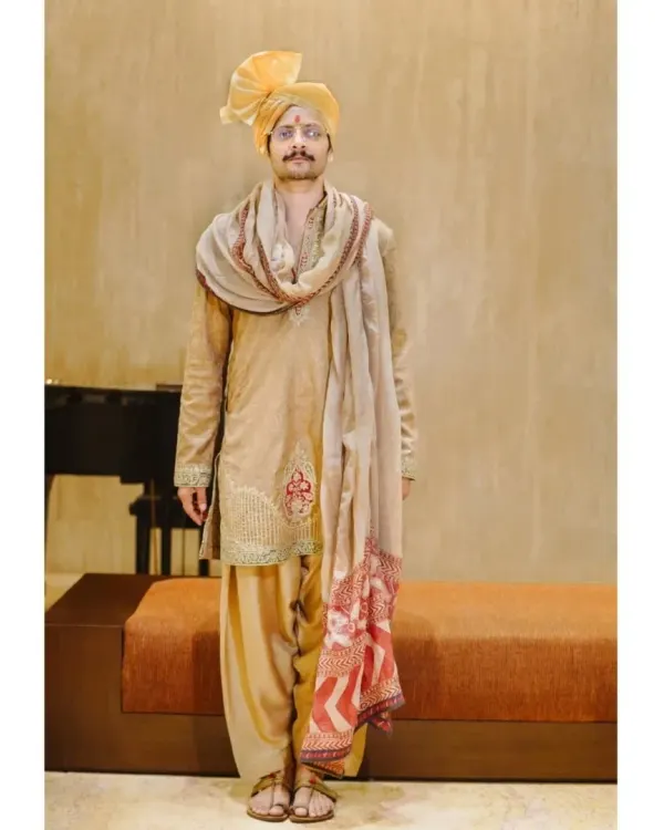 A classic, full-length portrait of the groom. His confident stance and traditional attire, complete with a vibrant yellow turban, are captured against a simple, elegant backdrop.