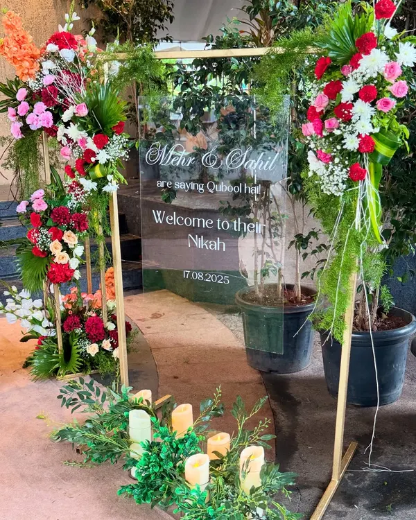 A modern and elegant welcome sign for Mehr and Sahil's Nikah, printed on a clear acrylic board and framed with beautiful, vibrant floral arrangements.