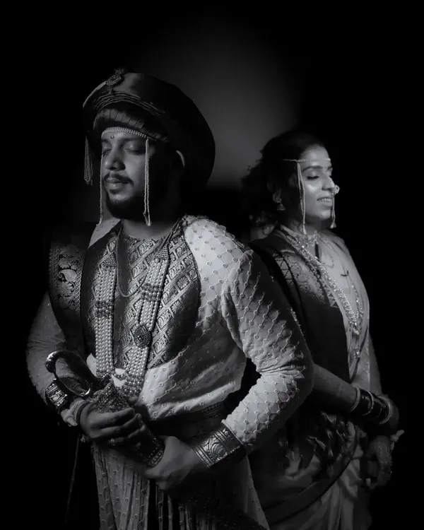 A powerful, royal-themed black and white portrait of a couple in traditional Peshwai attire, emphasizing their regal presence and the rich textures of their outfits.