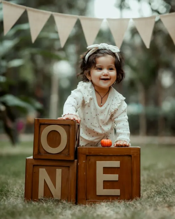 A joyful first birthday portrait of a baby girl with "ONE" blocks. Her happy expression and the rustic outdoor setting make this a perfect milestone photo.