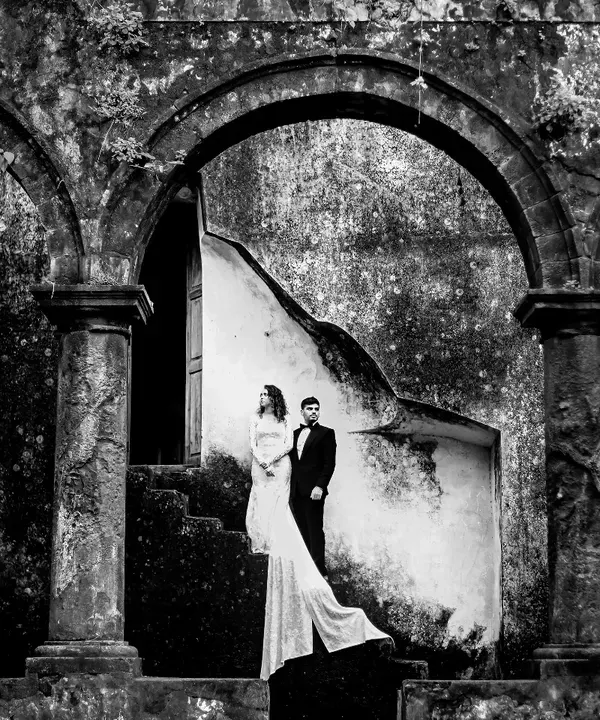 A black and white portrait that uses the strong arches of the ruins to frame the couple. The high contrast and shadows create a timeless, dramatic feel, focusing purely on their presence and the historic atmosphere.