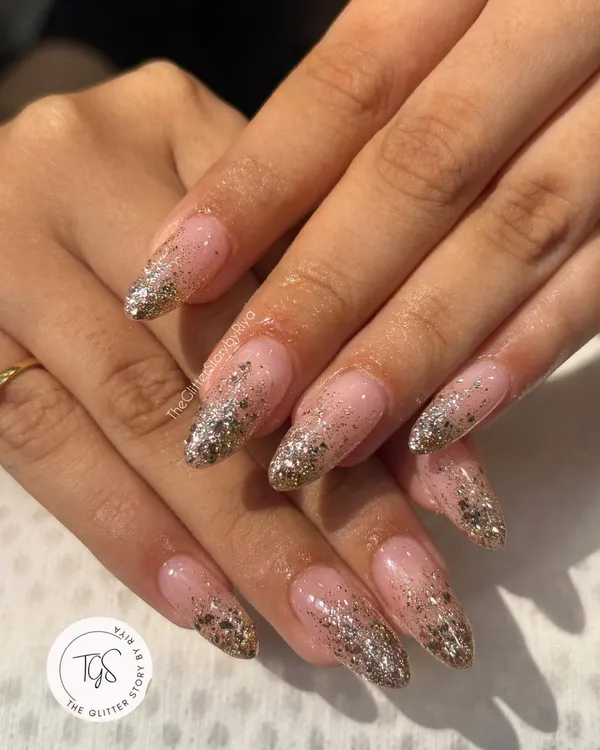 A full-on glamour set with a silver and gold glitter fade. These long, almond-shaped nails feature a nude base that transitions into a dense, sparkling glitter tip.