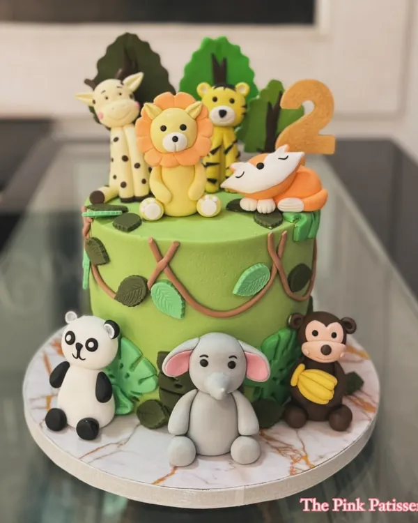 A vibrant jungle theme cake for a second birthday, surrounded by handcrafted fondant animals. A friendly lion, tiger, panda, elephant, monkey, and giraffe gather for a wild celebration.