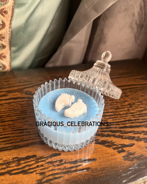A beautiful baby boy announcement candle in a crystal jar. The wax is colored blue and topped with tiny baby feet embeds, making it a super cute and affordable favor.