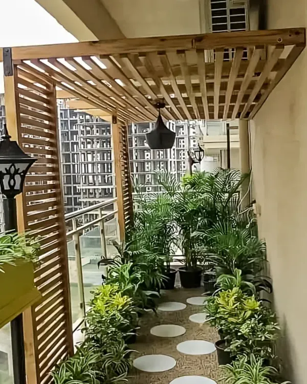 A charming balcony featuring a wooden pergola with hanging lanterns. The space is filled with potted plants, creating a private and lush garden feel in an urban setting.