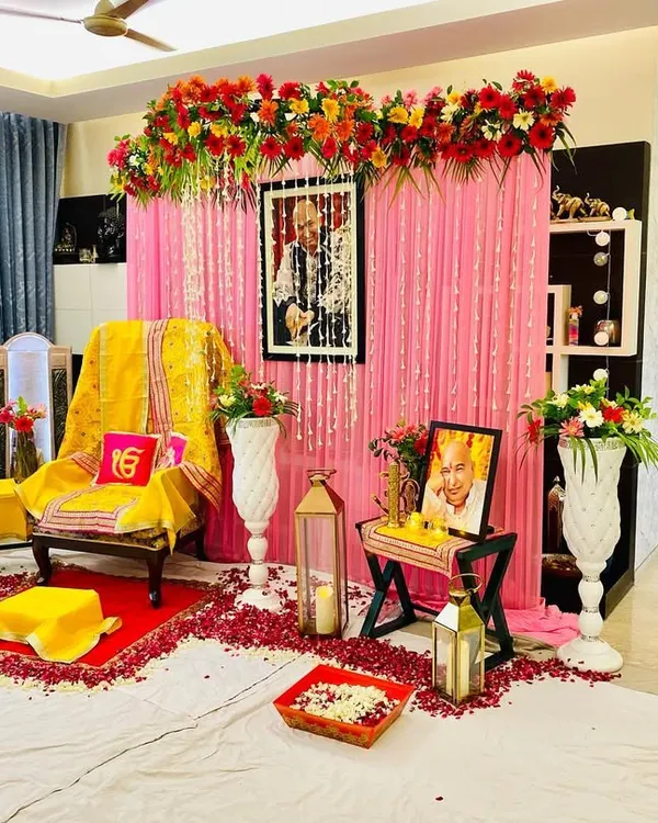 I create complete setups for Guruji satsangs at home. This one shows a main aasan with a yellow shawl, a pink curtain backdrop with a floral arrangement, and lanterns with rose petals for a blessed atmosphere.