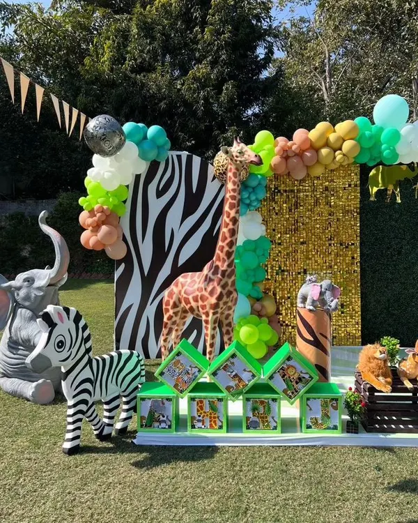 A fantastic outdoor jungle safari photo booth with a gold sequin wall, zebra-print panel, and life-sized giraffe, zebra, and elephant props.