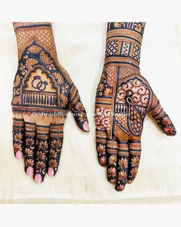A classic bridal design featuring engagement rings under a royal arch on one hand and a majestic peacock on the other. The patterns are dense with lotus flowers and geometric checks.