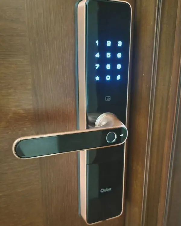 A close-up of a newly installed Qubo smart door lock. Notice the illuminated touch keypad and the integrated fingerprint sensor on the handle for quick, one-touch access.