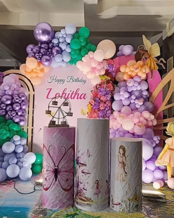 An elaborate fairy and butterfly themed birthday for Lohitha. This enchanting setup features a rainbow of pastel balloons, fairy wing props, and custom-printed plinths with magical illustrations.
