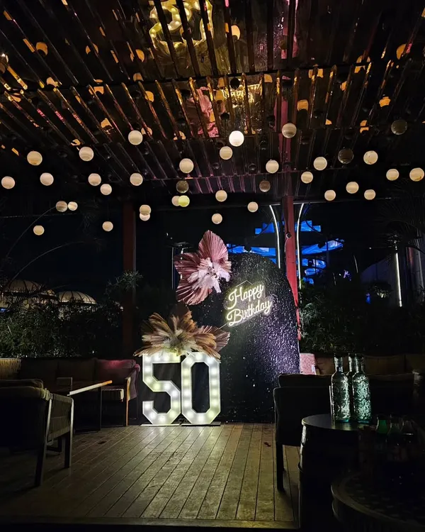 A stunning 50th birthday setup on a rooftop with warm string lights, a black sequin backdrop, and large marquee numbers. This decor creates a sophisticated and celebratory party atmosphere.