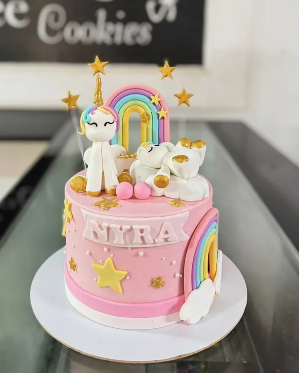 A magical unicorn and rainbow cake. This pink cake is adorned with a fondant unicorn, rainbows, stars, and a sleeping bear on a cloud.