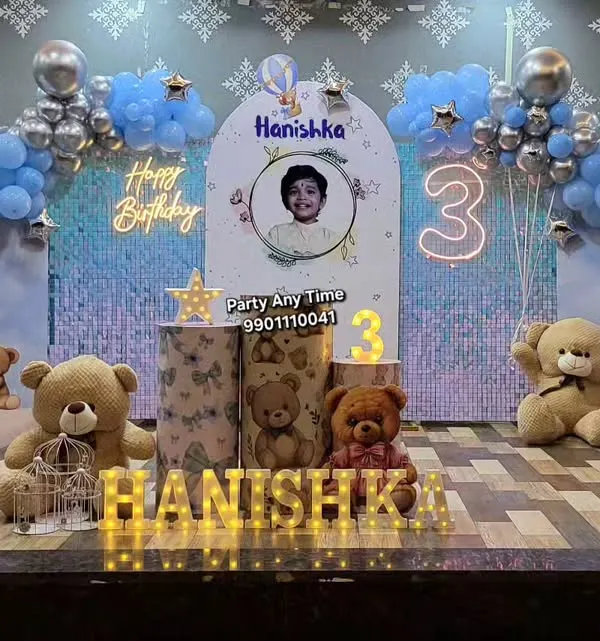 A complete teddy bear theme for a 3rd birthday. This setup includes a shimmer wall, moon prop, custom backdrop, themed plinths, and light-up letters.