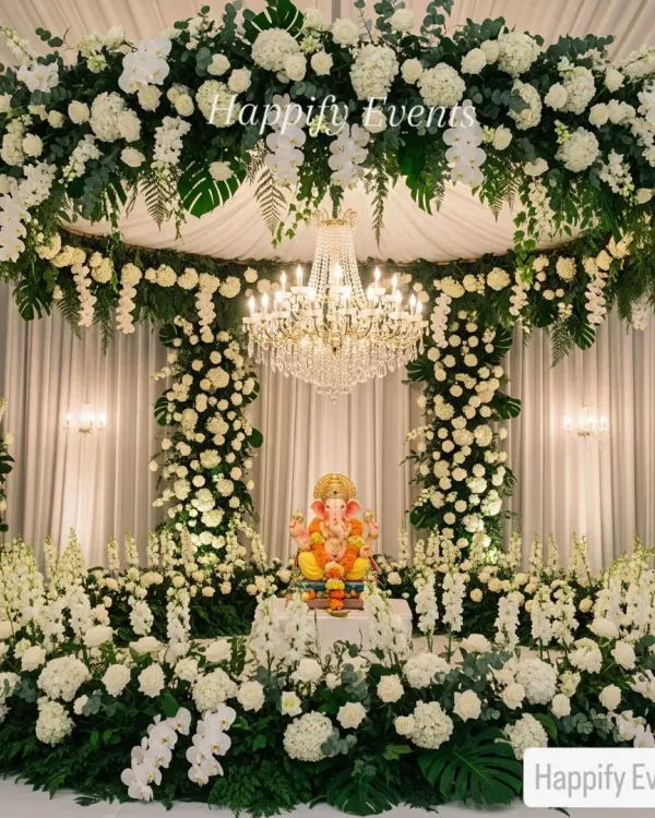 A breathtaking Ganpati mandap designed with a lush canopy of white roses, hydrangeas, and cascading orchids. The setup is illuminated by a grand crystal chandelier, creating a divine and opulent atmosphere for welcoming Bappa.