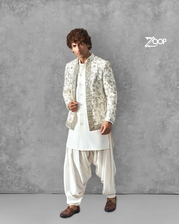 A classic groom's look featuring an intricately embroidered jacket over a pristine white pathani salwar. This outfit is designed for the man who appreciates timeless elegance and superior craftsmanship for his wedding day.