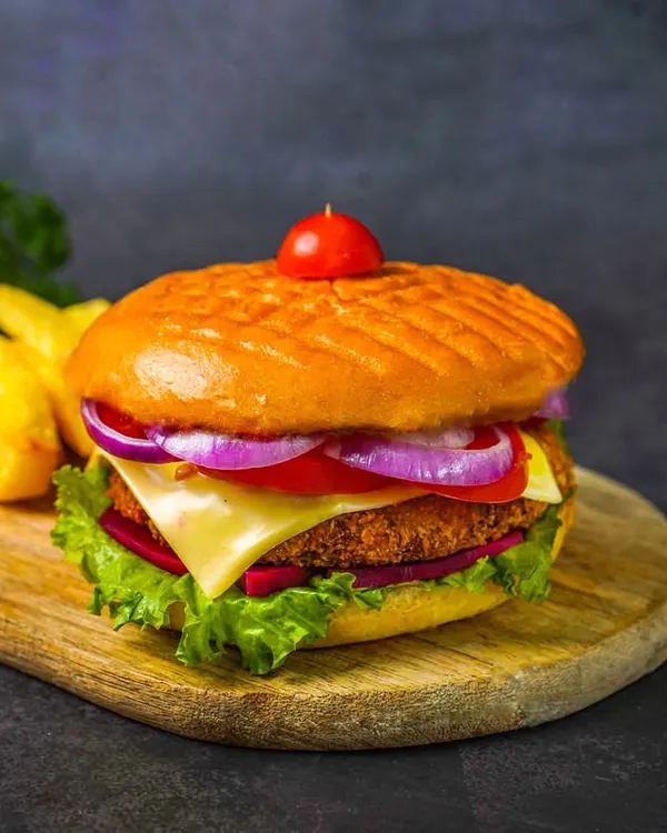 A picture-perfect burger with a veggie patty, cheese, lettuce, tomato, and onion, served with fries on a wooden board against a dark background.