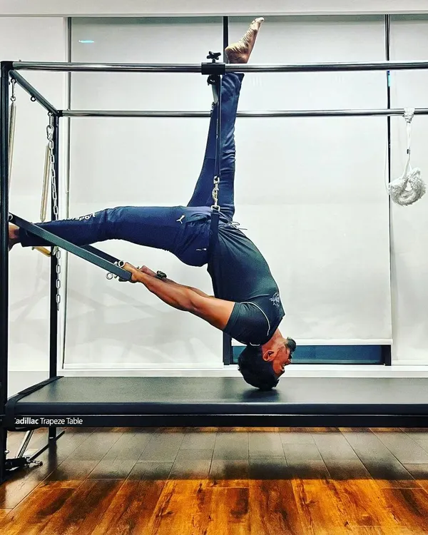 An unbending tree is easily broken. This advanced inverted stretch on the Cadillac Trapeze Table is a testament to the power of flexibility. This pose helps decompress the spine and requires significant core control and strength.