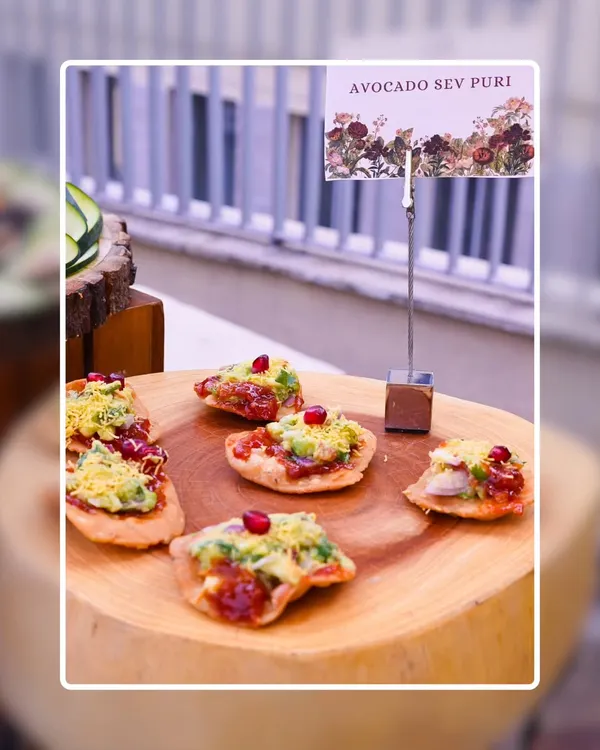 Our Avocado Sev Puri is a modern take on a classic chaat. Crispy puris are topped with fresh avocado, tangy chutneys, and pomegranate seeds, served on a rustic wooden platter.