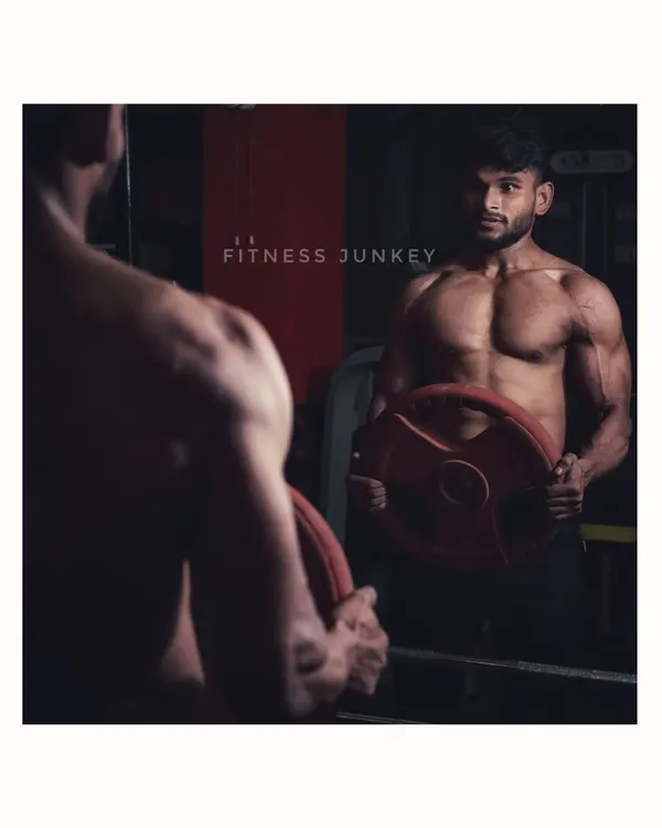A classic shot for a bodybuilding portfolio, using a mirror to capture both the reflection and the subject. The dramatic lighting highlights the muscle definition in the back and arms while holding a weight plate.