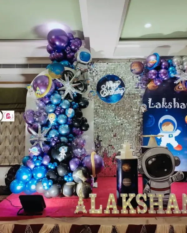 A complete outer space themed birthday party for Lakshan. This grand setup includes a shimmering silver backdrop, a galaxy balloon garland, astronaut cutouts, and a large light-up number '6'.