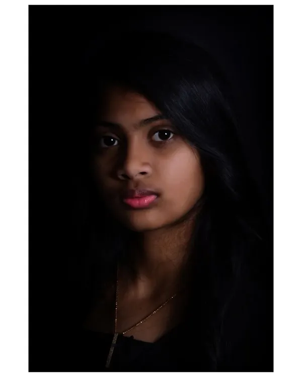 A dramatic, low-key portrait of a young woman. This style of lighting creates a moody and artistic feel, highlighting facial features in a subtle way.