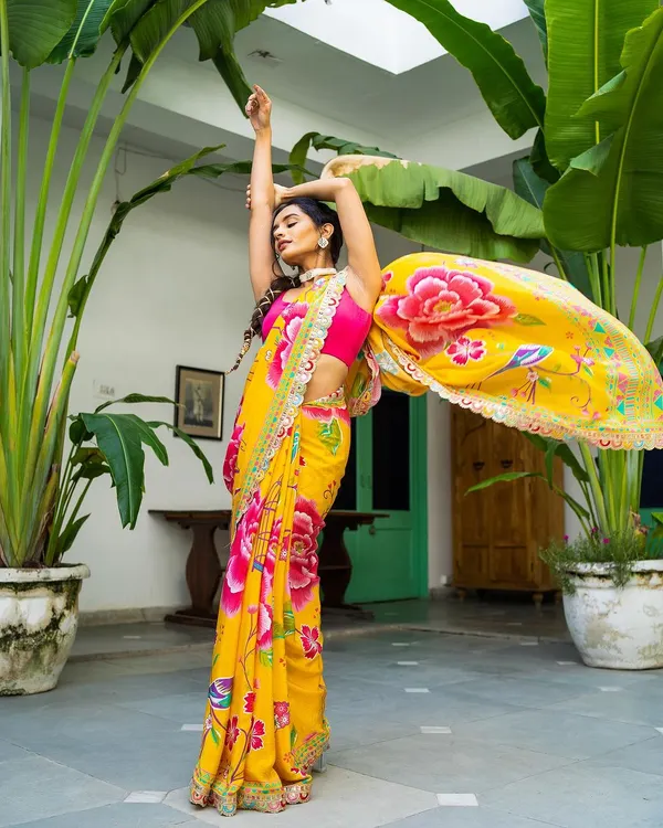 A moment of pure energy and color. The model's pose sends the vibrant yellow floral saree flying, creating a beautiful arc of fabric against the lush green background. This is what capturing a story looks like.