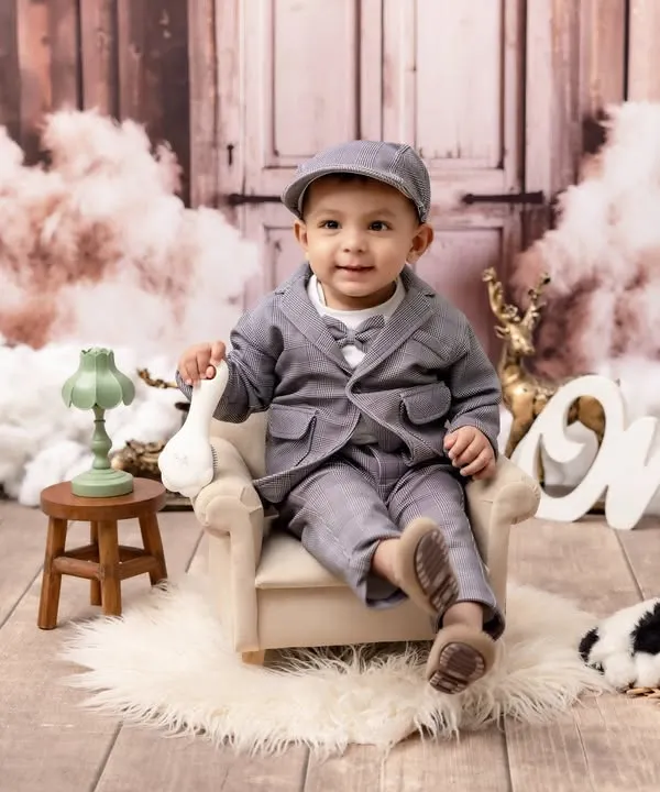 Celebrating one year of life with style and personality. This little gentleman is dressed in a dapper suit for his first birthday photoshoot, set against a classic, rustic backdrop that makes his big milestone feel even more special.