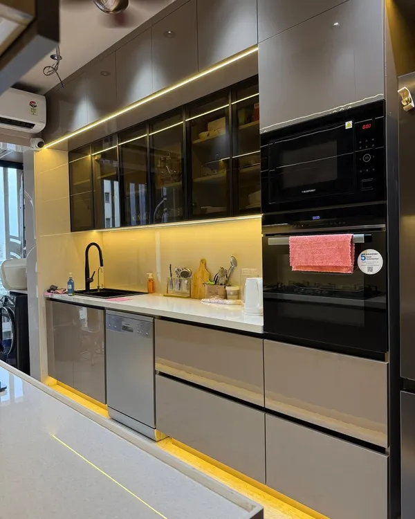 This modern parallel kitchen in a Mumbai suburb is one of my favorite recent projects. I used a combination of Roasted Chestnut laminate and tinted glass for the cabinets, creating a warm yet sleek look. The design features fully integrated Blaupunkt appliances and a durable quartz countertop, all illuminated by layered profile lighting to make the space feel both functional and luxurious.