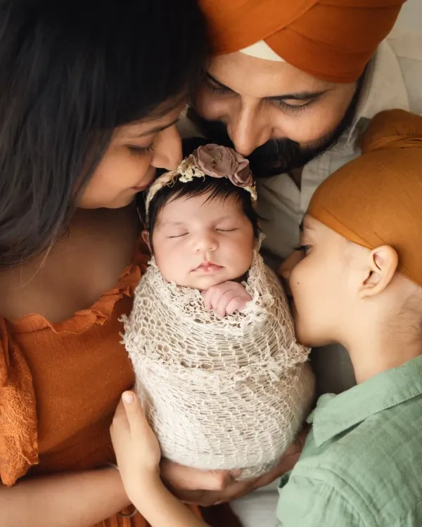 A beautiful close-up of a family of four, with both parents and a big brother kissing the newborn baby. This is a classic pose for a newborn with sibling photoshoot.