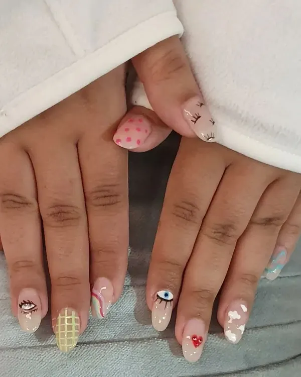 A fun, mismatched manicure showcasing a variety of hand-painted designs, including evil eyes, clouds, hearts, and geometric patterns.
