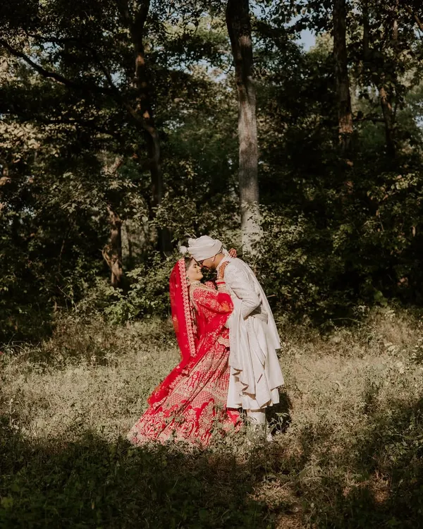 A romantic kiss in the middle of a forest in Austin, Texas. The bride's vibrant red lehenga against the green woods creates a stunning, fairytale-like image.