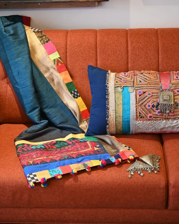 A custom-made Banjara throw and lumbar cushion set, designed to add a burst of festive color. The vintage Banjara textile is richly embellished with old jewelry, coins, and tassels, turning it into a statement piece for the sofa.