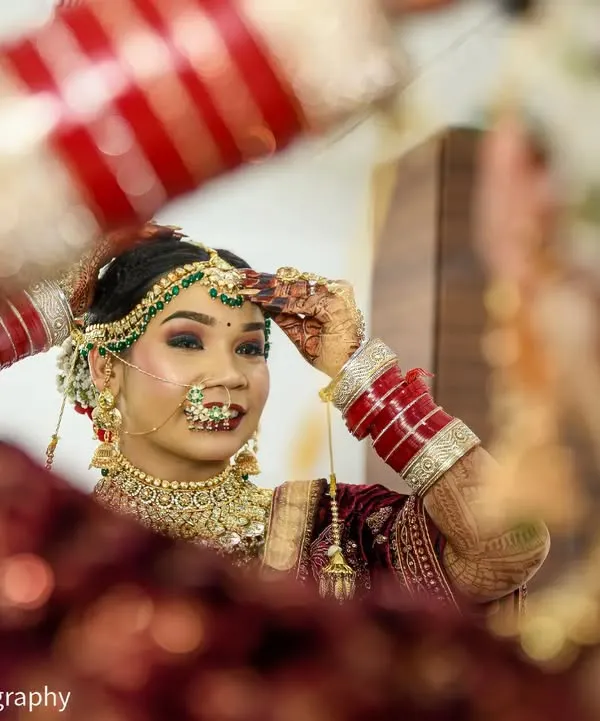 Capturing the final touches. This Punjabi bride, dressed in a stunning Sabyasachi lehenga, adjusts her jewelry while looking in the mirror, a beautiful moment of anticipation on her wedding day.